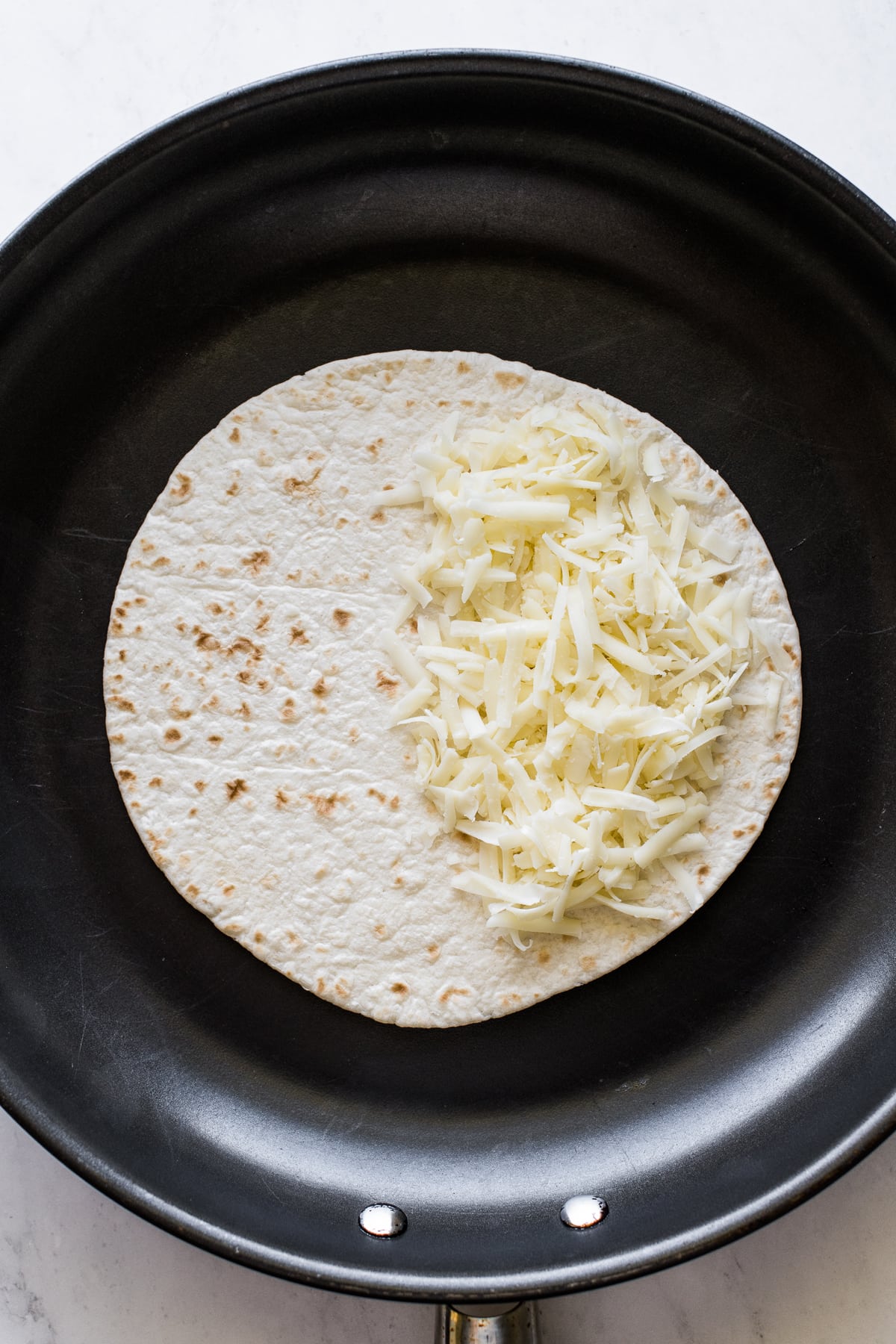 A flour tortilla in a skillet with shredded cheese.