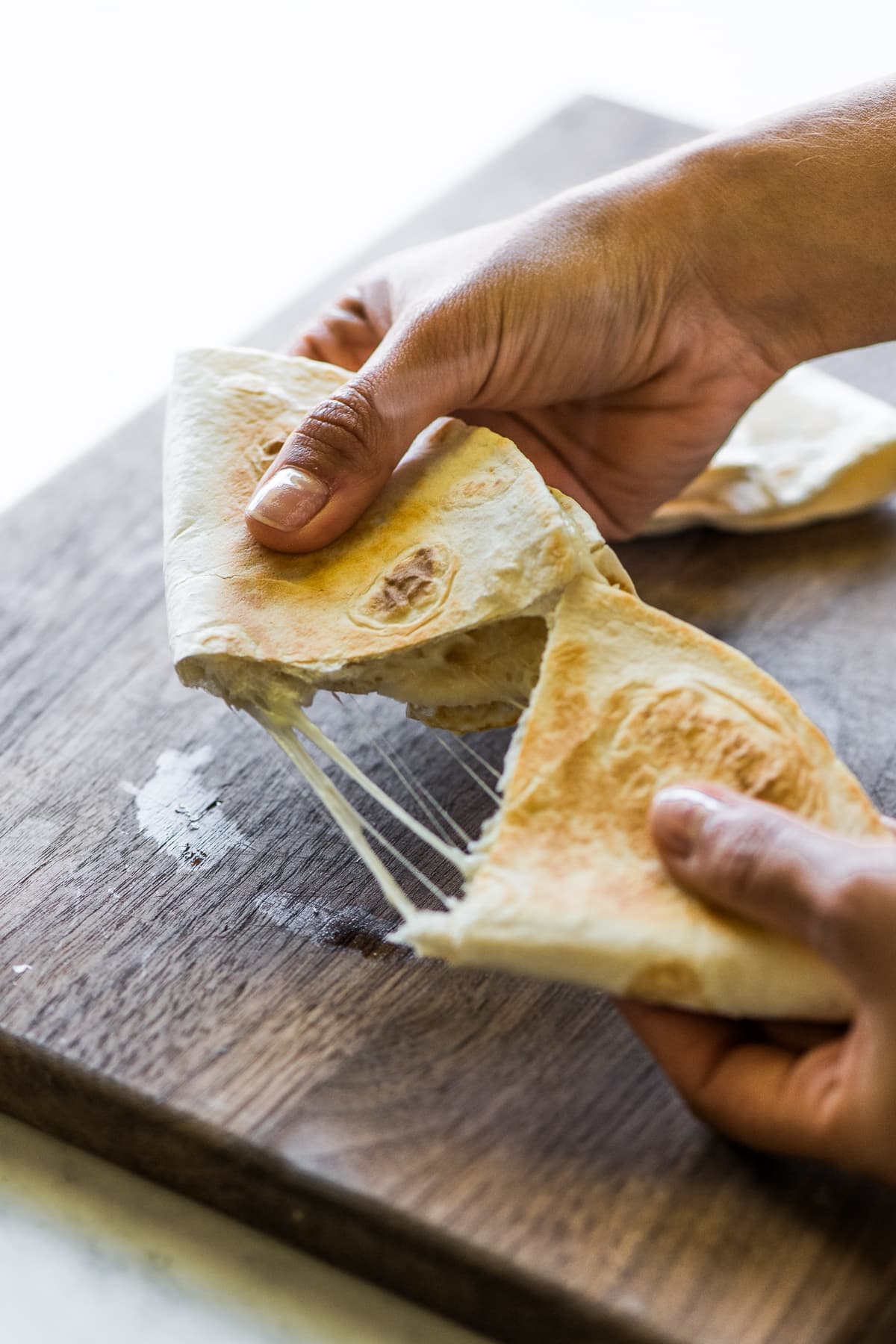 A cheese quesadilla being pulled apart, revealing melted stretchy cheese.