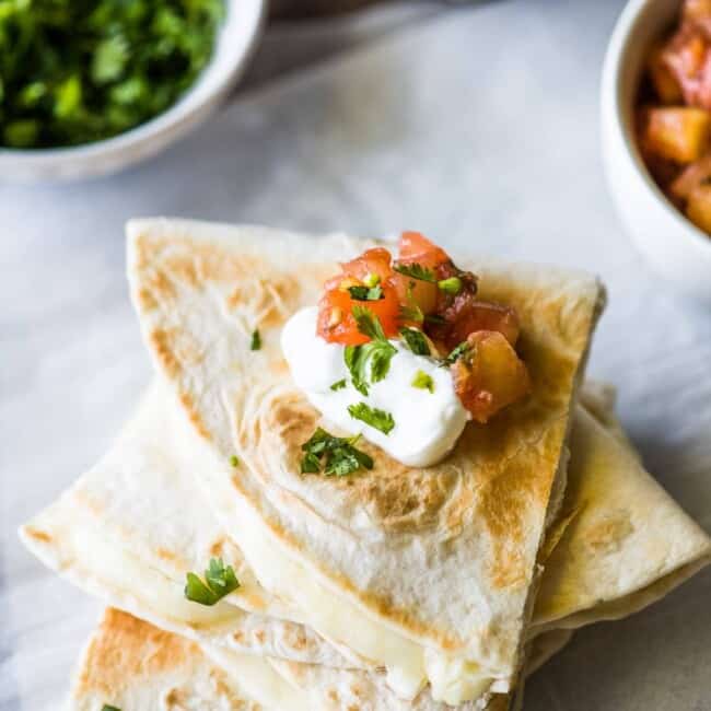 A cheese quesadilla topped with sour cream and pico de gallo.