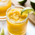A mango margarita served frozen with a lime wedge.