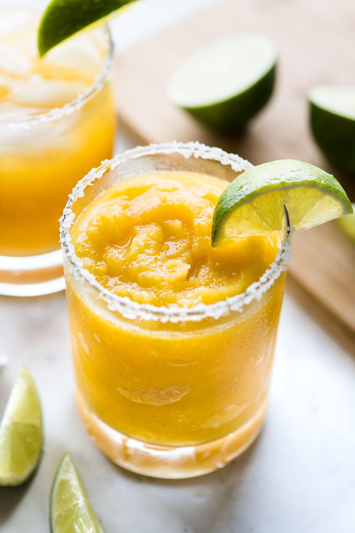 A mango margarita served frozen with a lime wedge.