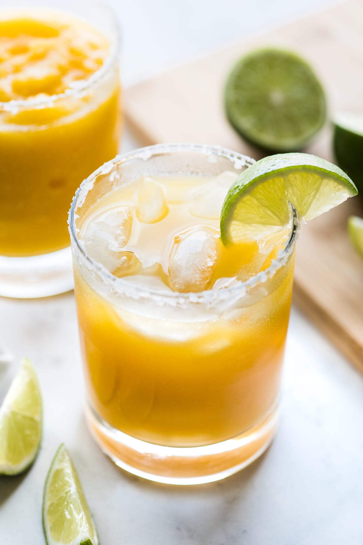 A mango margarita on the rocks with a lime wedge