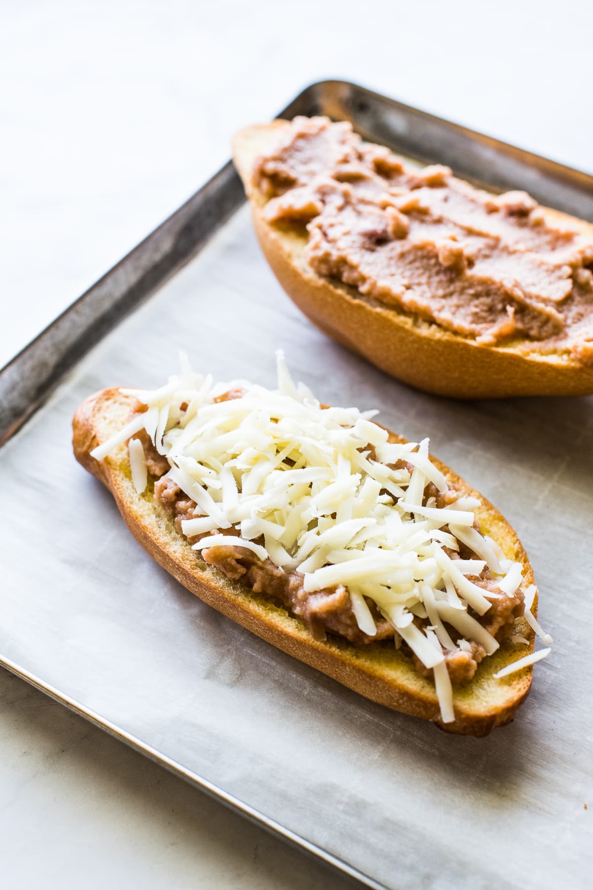 Toasted bolillo bread topped with refried beans and shredded cheese.