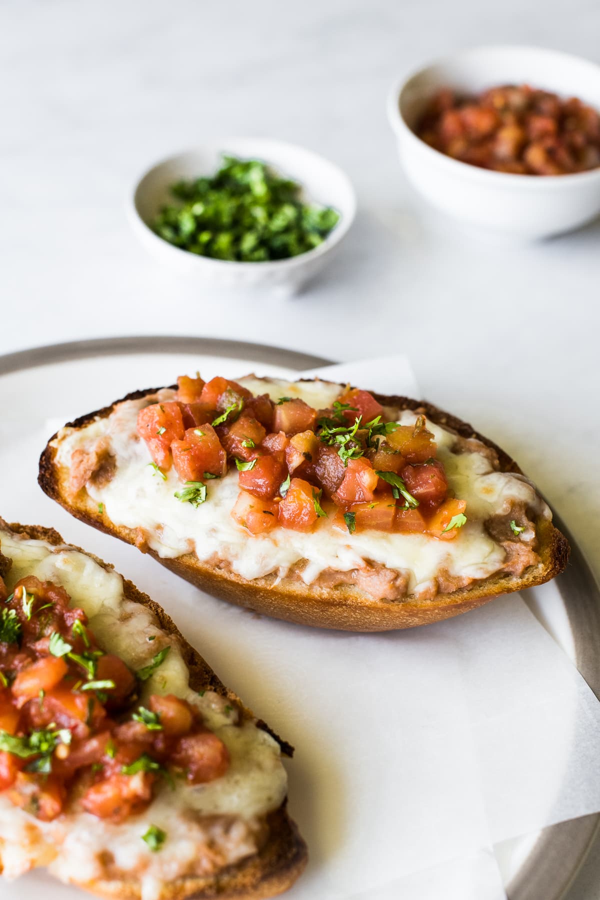 Molletes on a plate topped with pico de gallo.