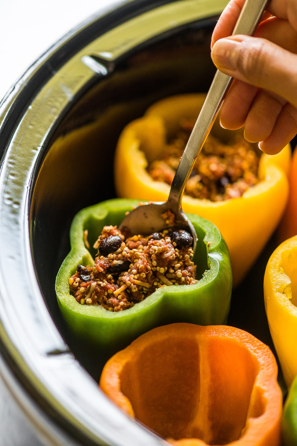 Bell peppers being stuffed with filling in a slow clooker.