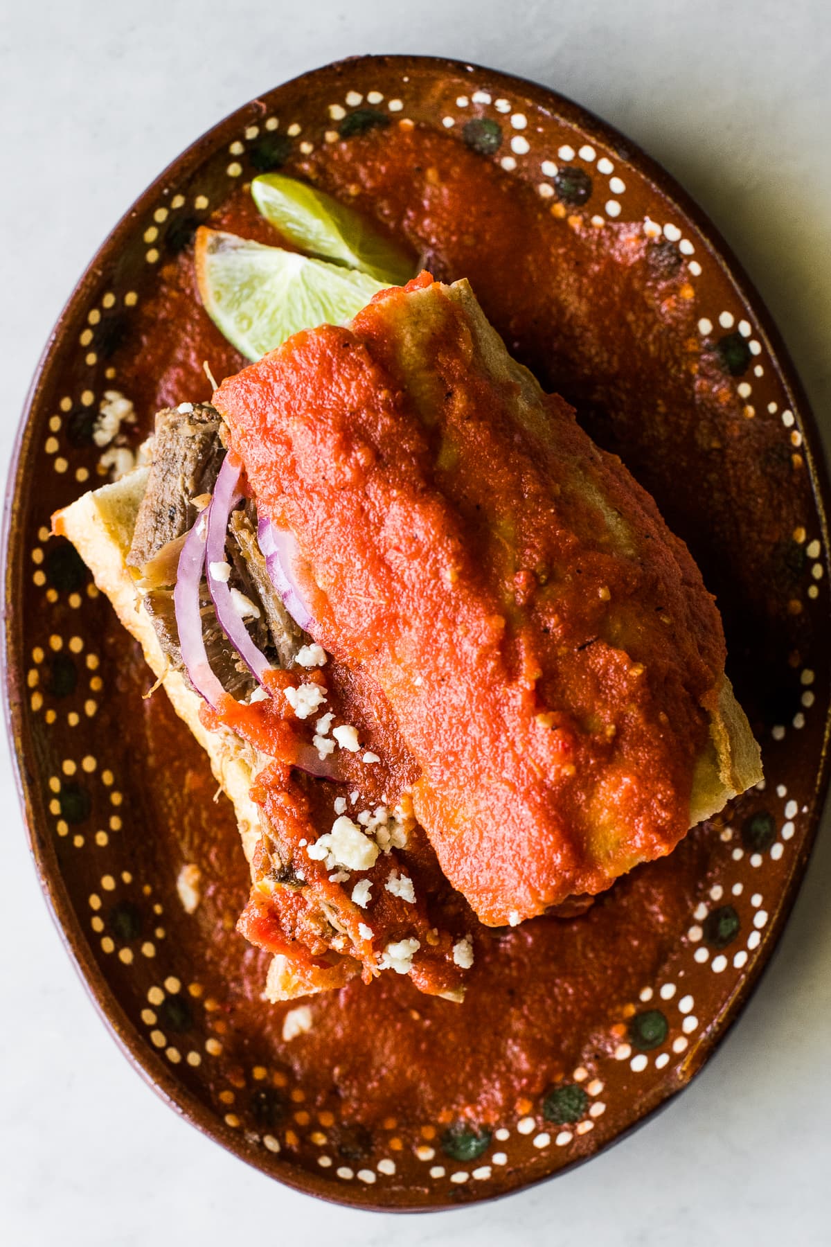 A torta ahogada Mexican sandwich on a traditional clay plate.