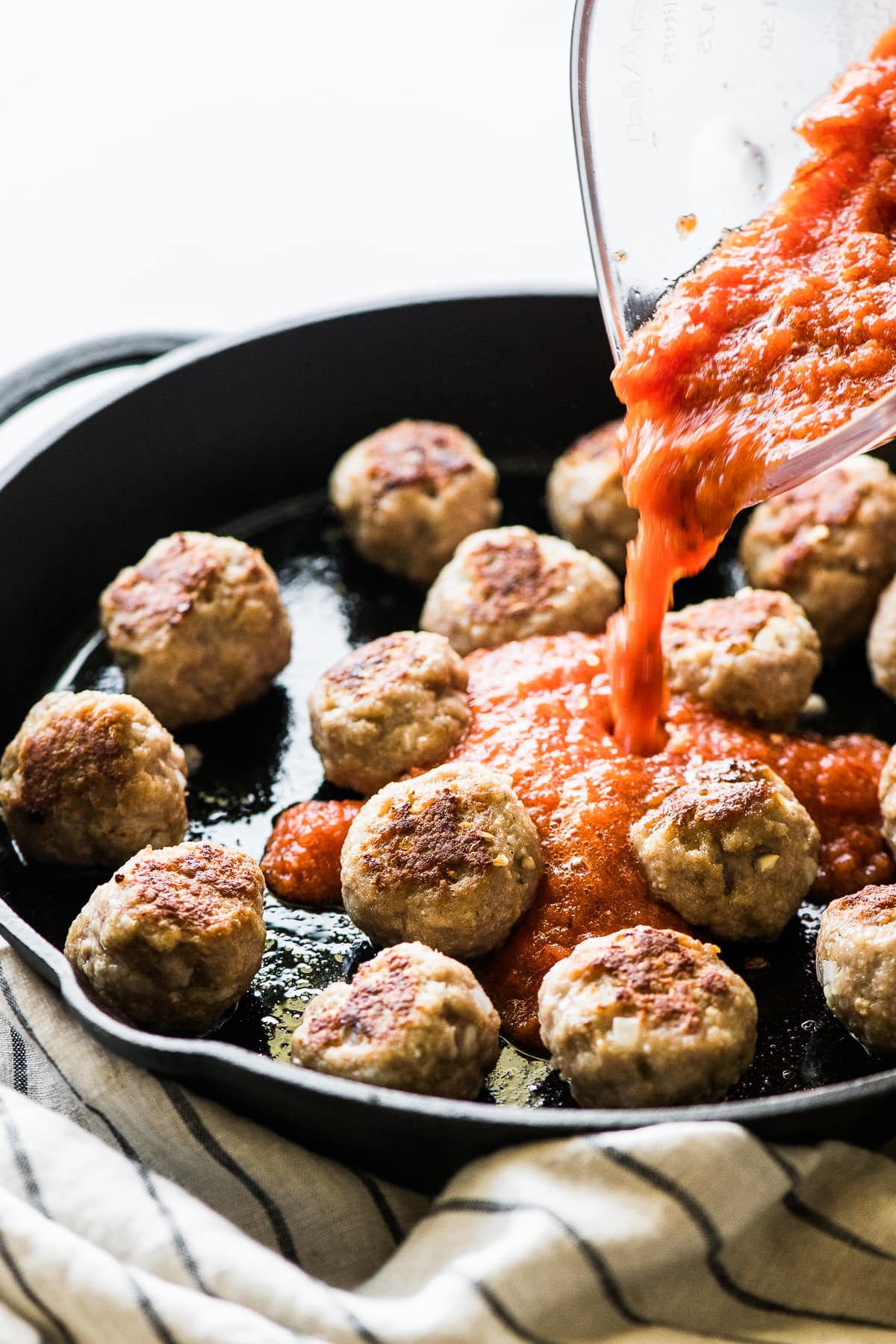 Mexican meatballs in a skillet with sauce being poured on top.