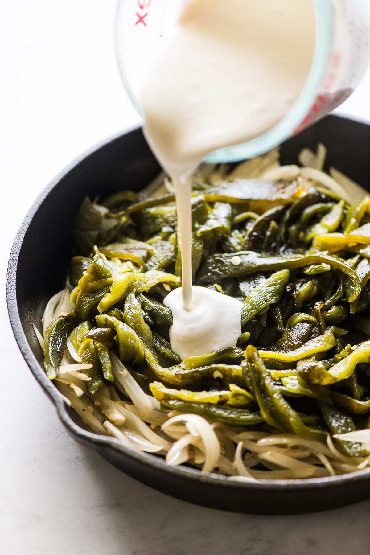 Mexican crema being poured on top of poblanos and onions.