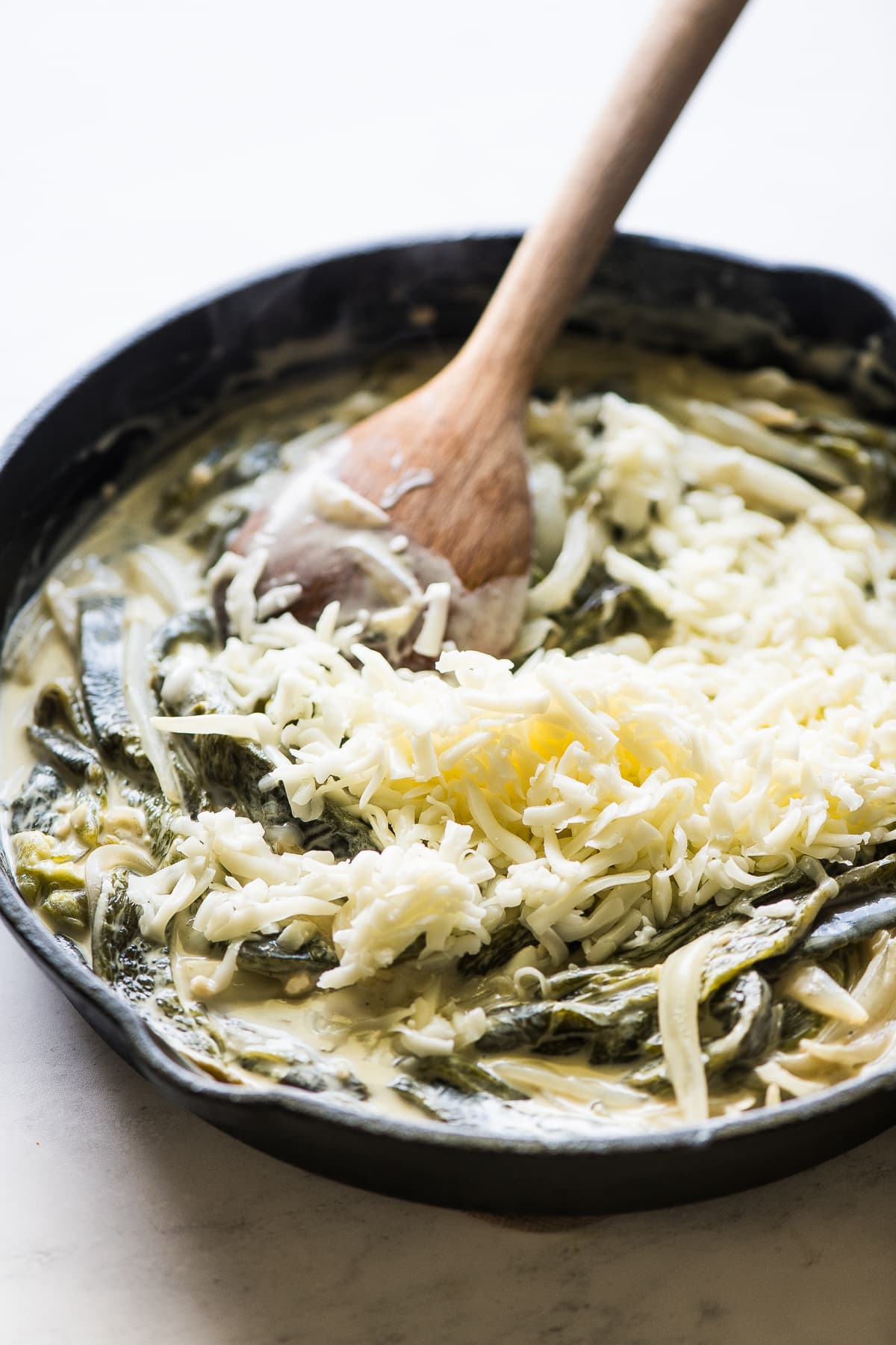 Shredded Oaxaca cheese being stirred into rajas con crema skillet.