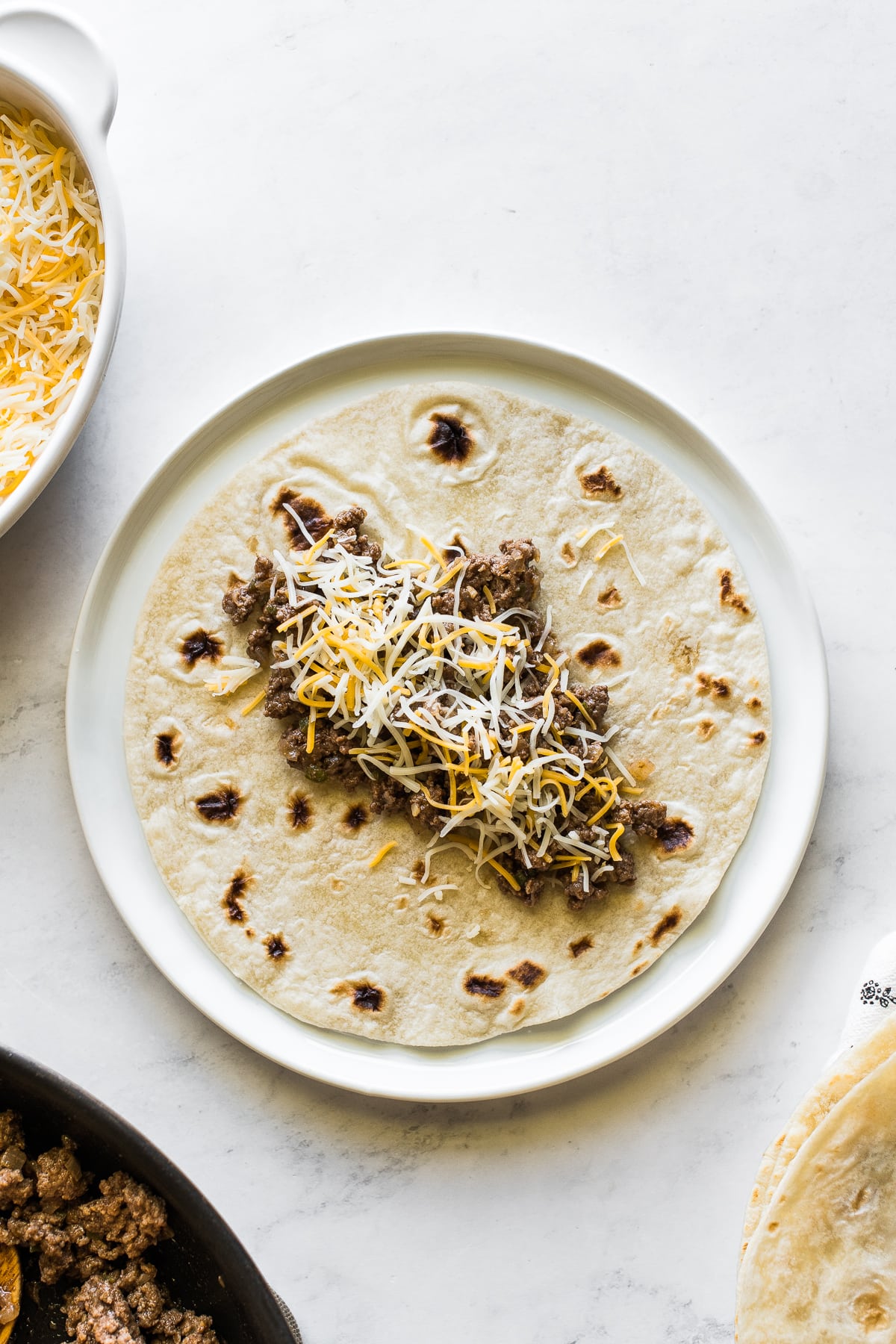 A flour tortilla with ground beef filling and shredded cheese on top.