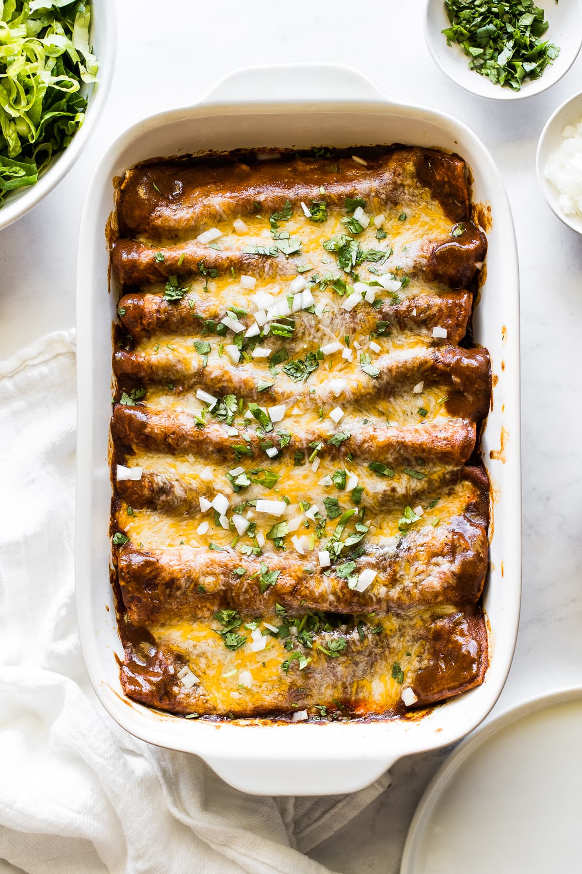 Ground beef enchiladas in a baking dish topped with cilantro and onions.