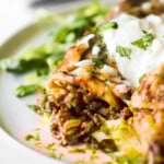 Beef enchiladas topped with sour cream on a bed of shredded lettuce.