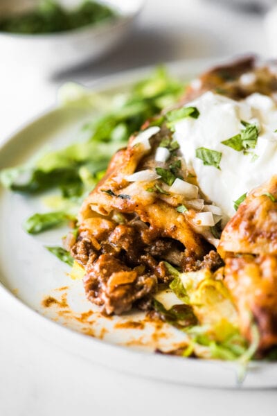 Beef enchiladas topped with sour cream on a bed of shredded lettuce.