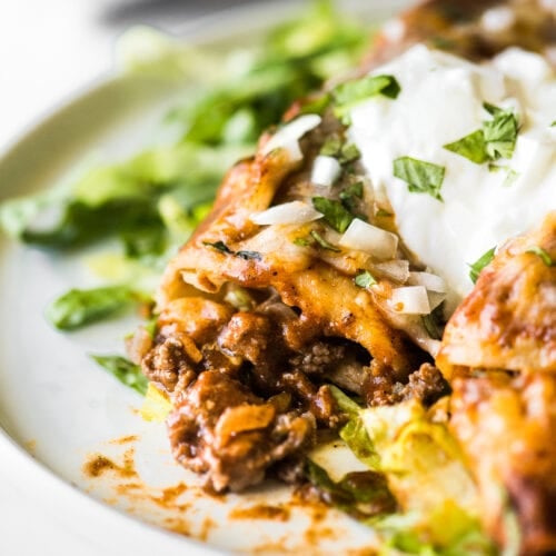 Beef enchiladas topped with sour cream on a bed of shredded lettuce.