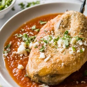 A chile relleno on top of a red tomato sauce on a plate.