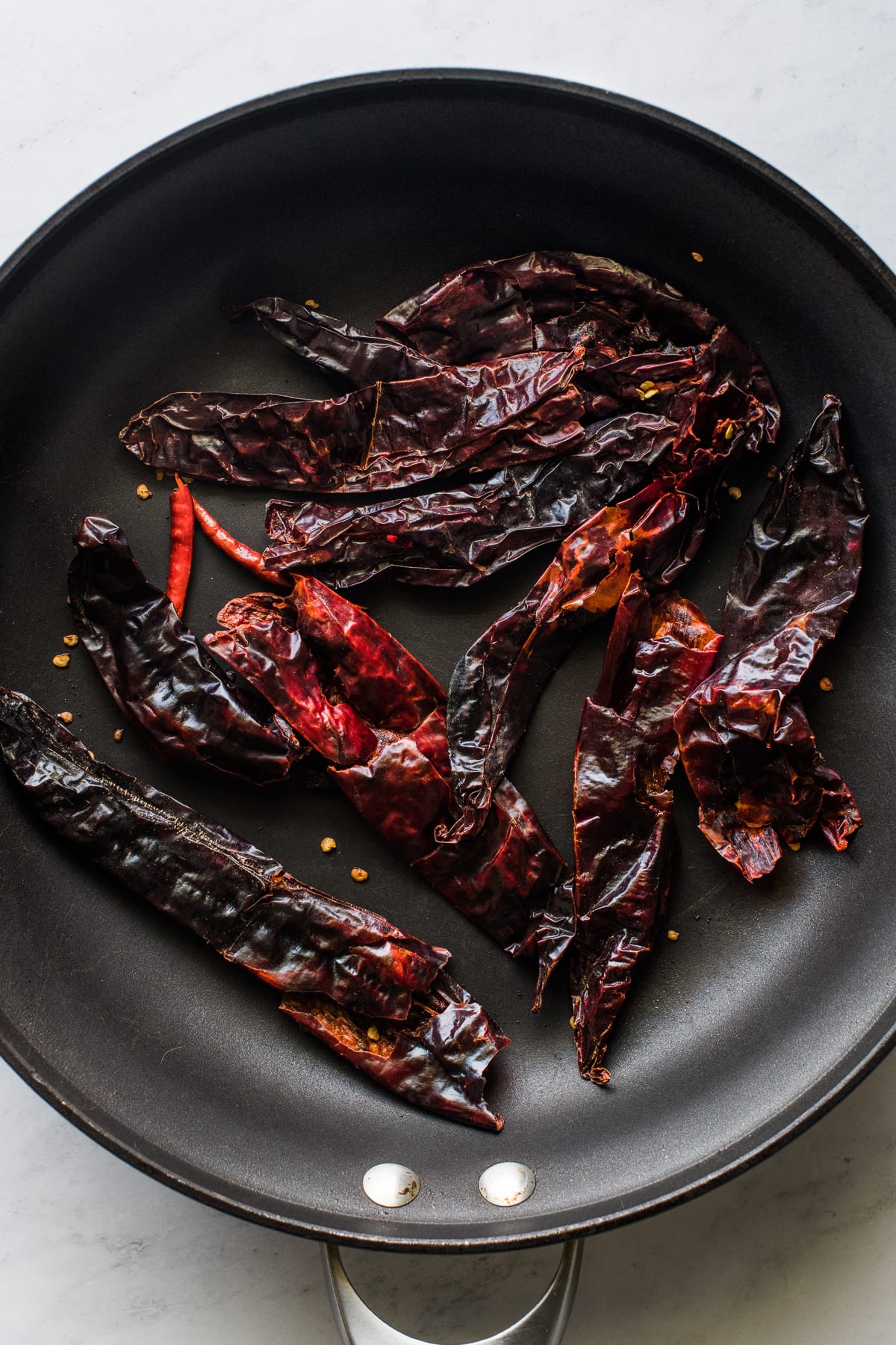 Guajillo chiles toasting on a skillet.