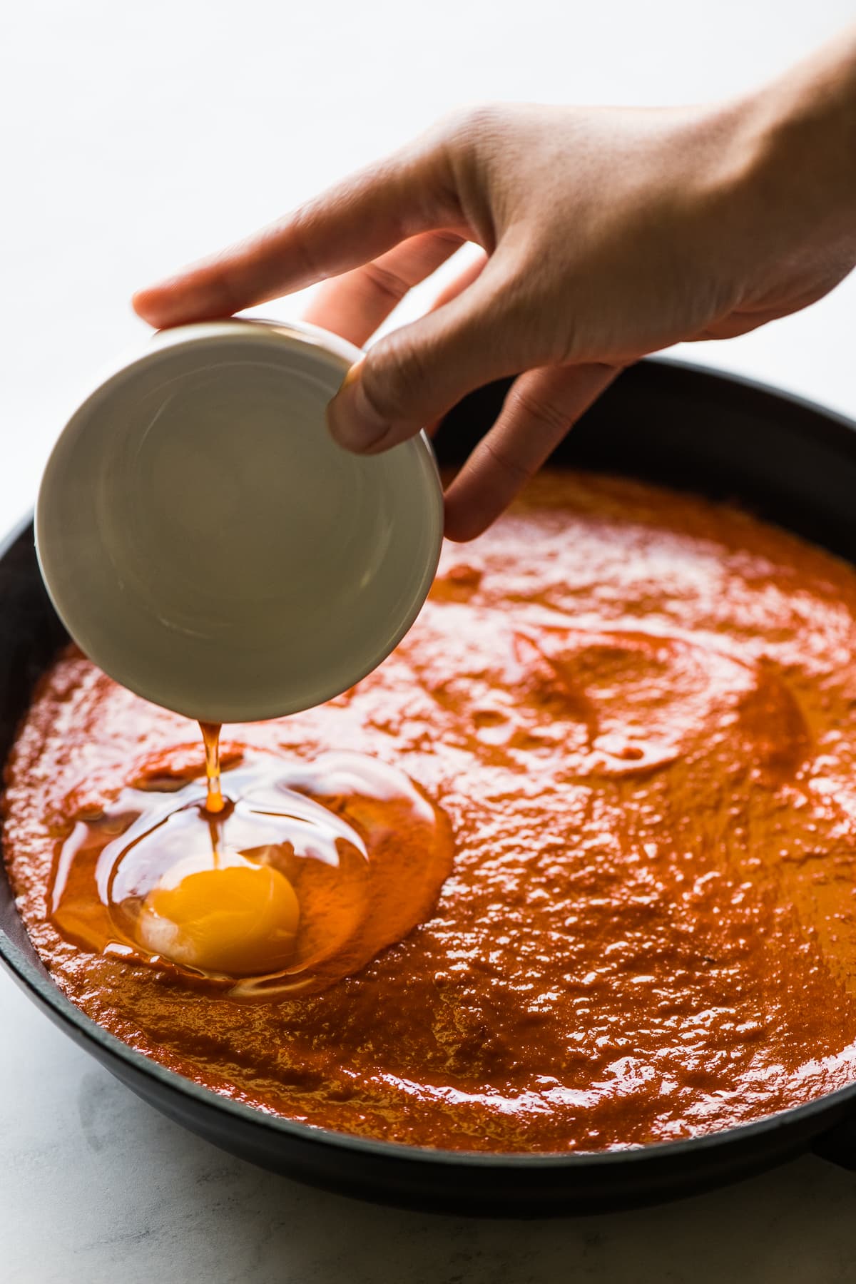 Um ovo sendo derramado em uma frigideira com salsa para huevos ahogados.