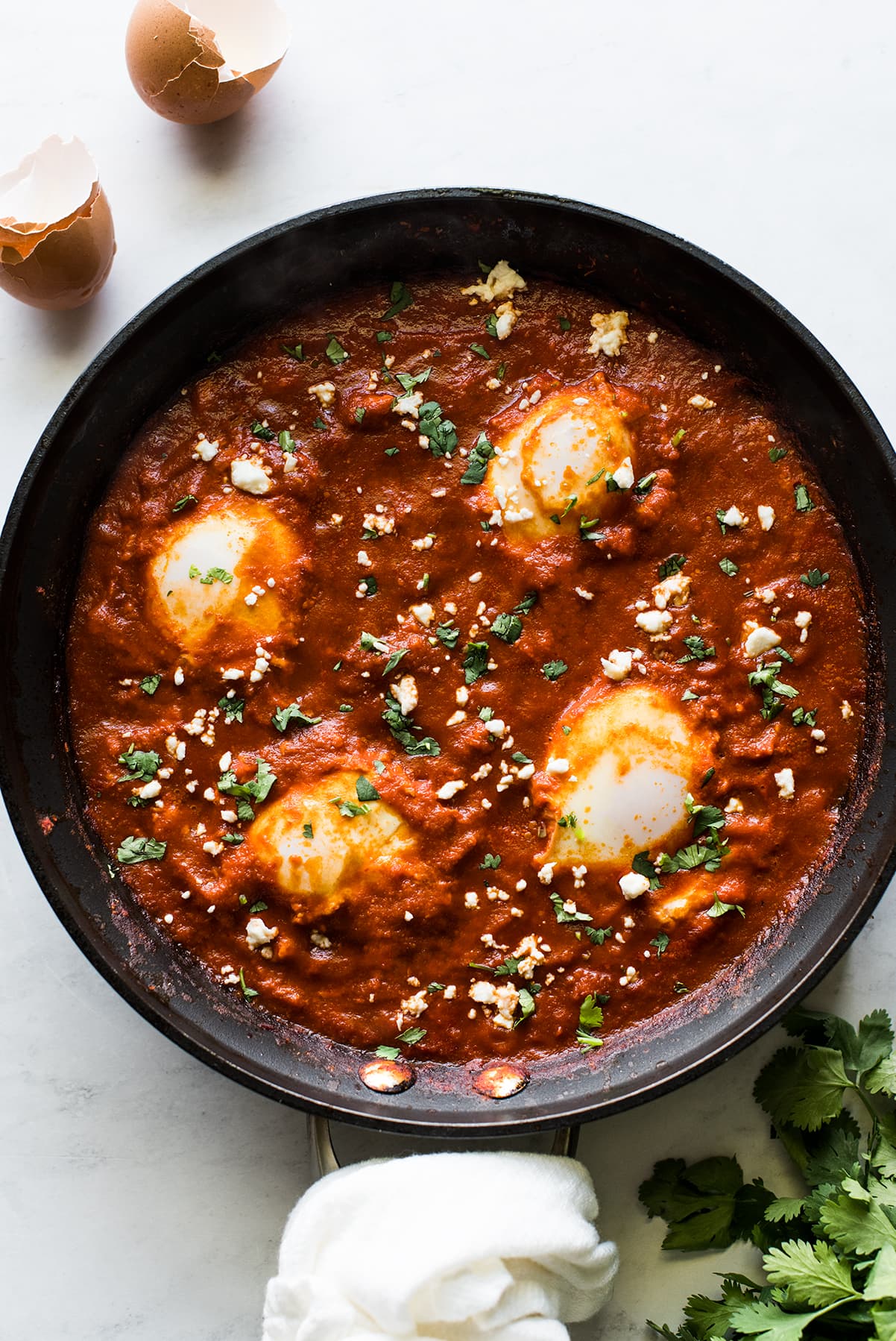 A skillet of huevos ahogados topped with cilantro and queso fresco.