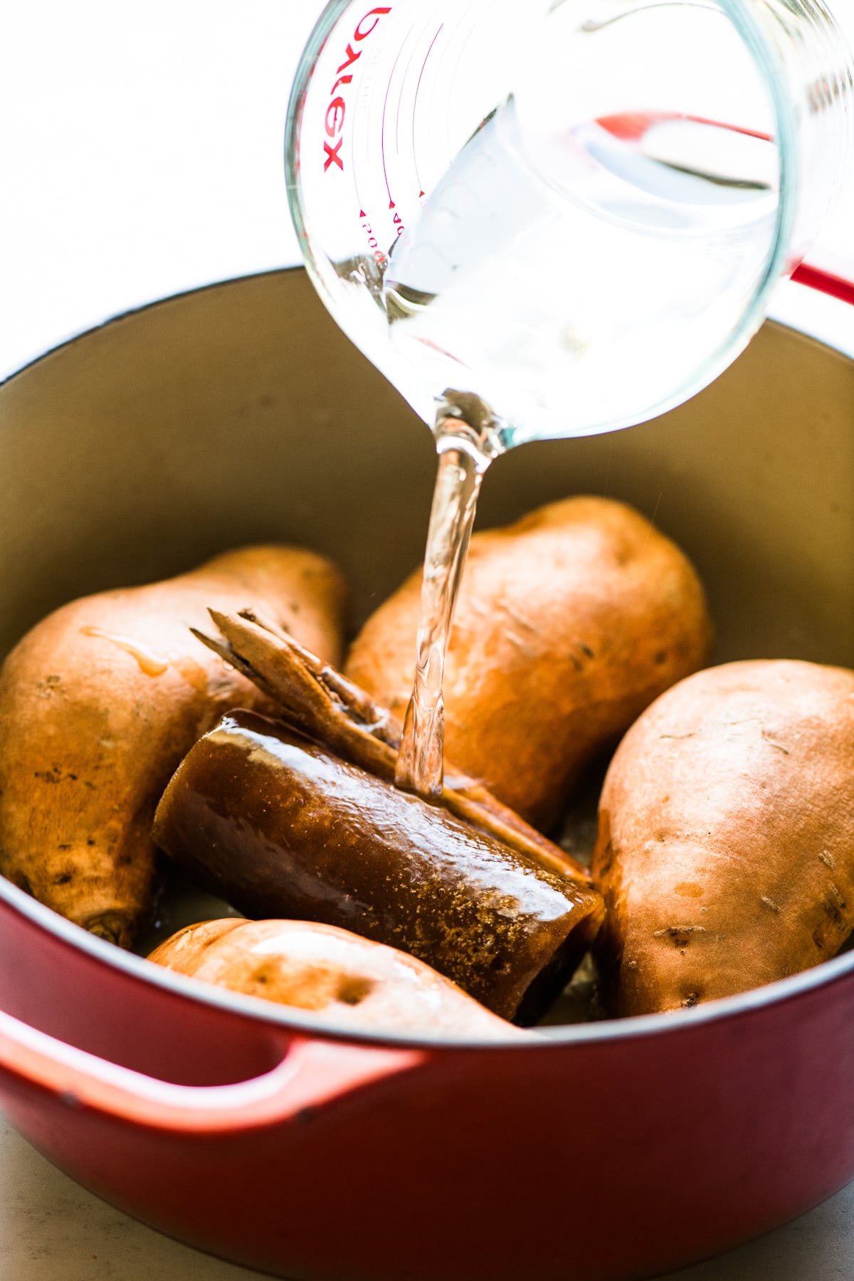 A dutch oven filled with sweet potatoes, piloncillo, and a cinnamon stick.