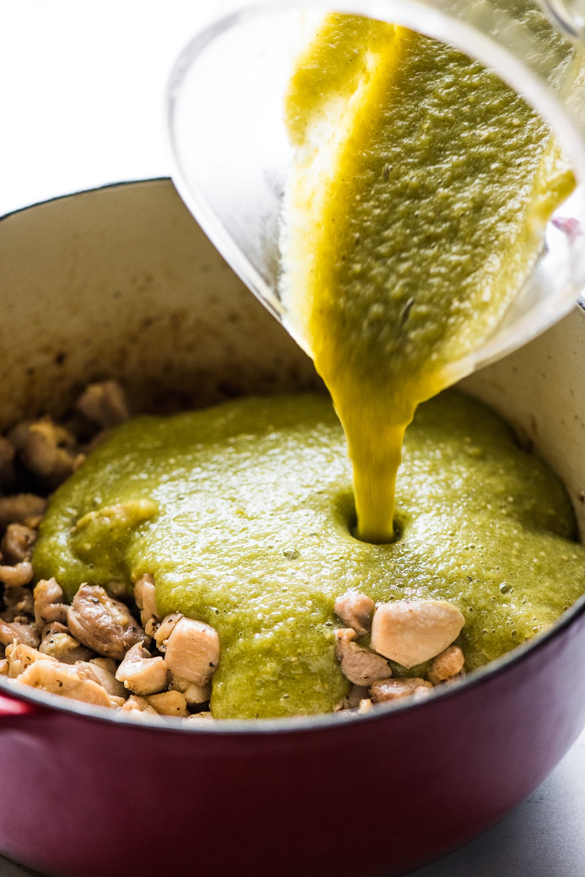 Green tomatillo sauce being poured on top of chicken in a pot.