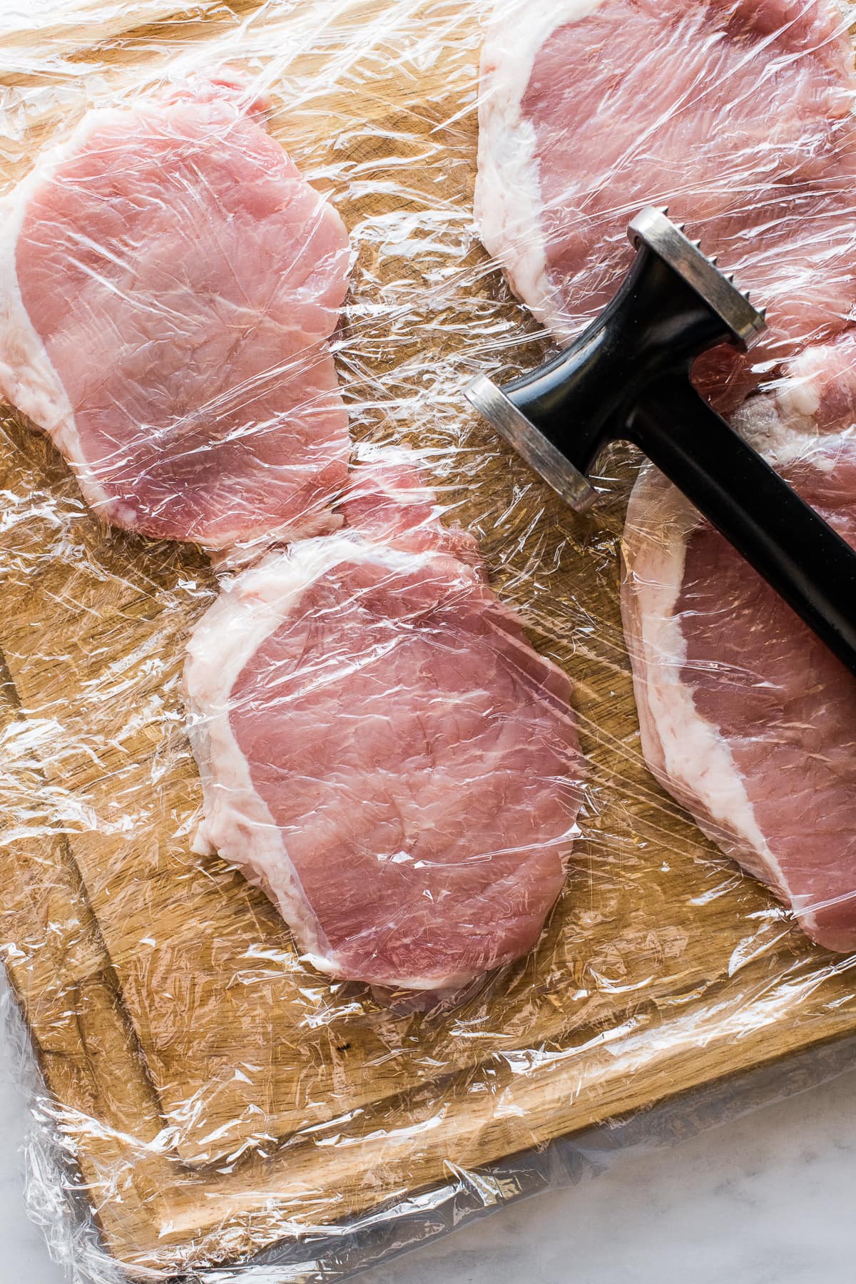 Boneless pork chops on a cutting board with a meat hammer.