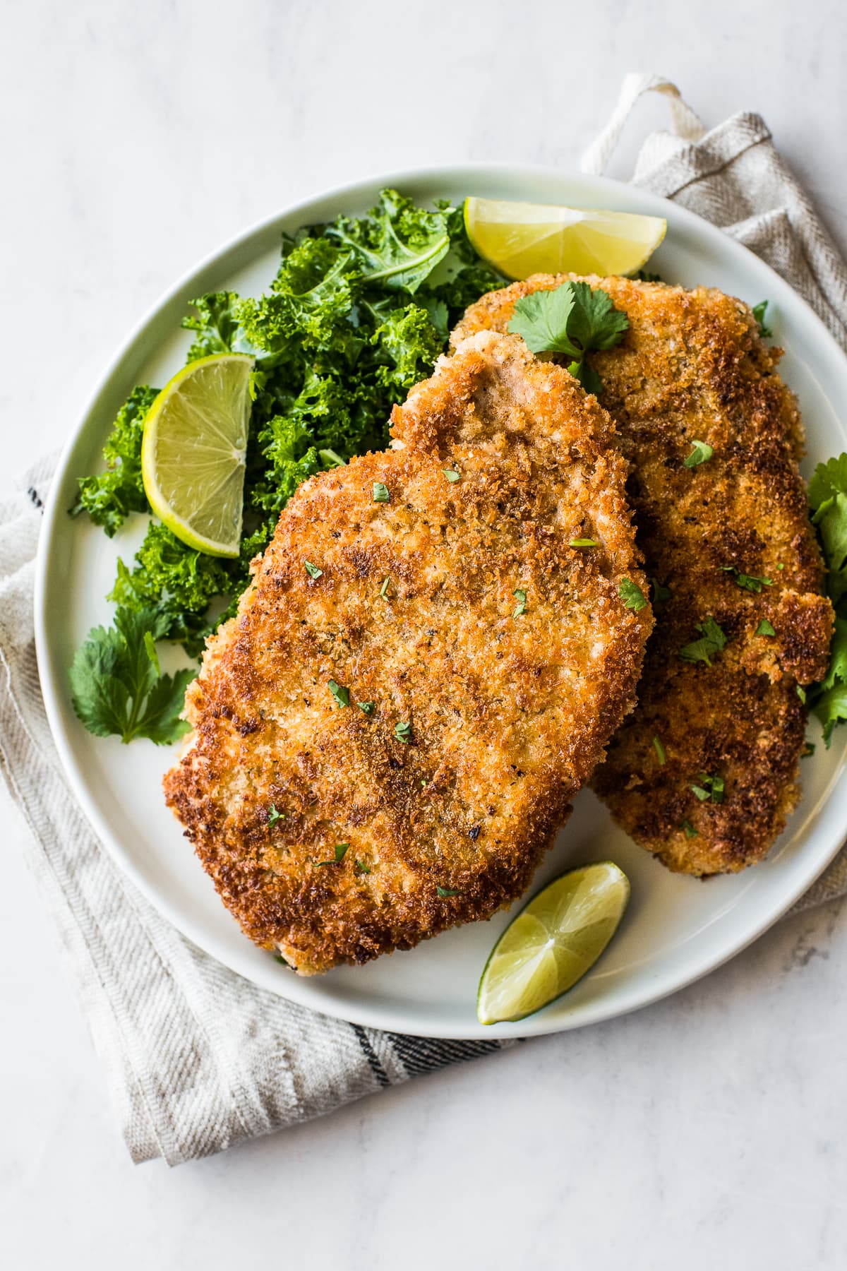 Crispy pork cutlets on a plate with lime wedges.