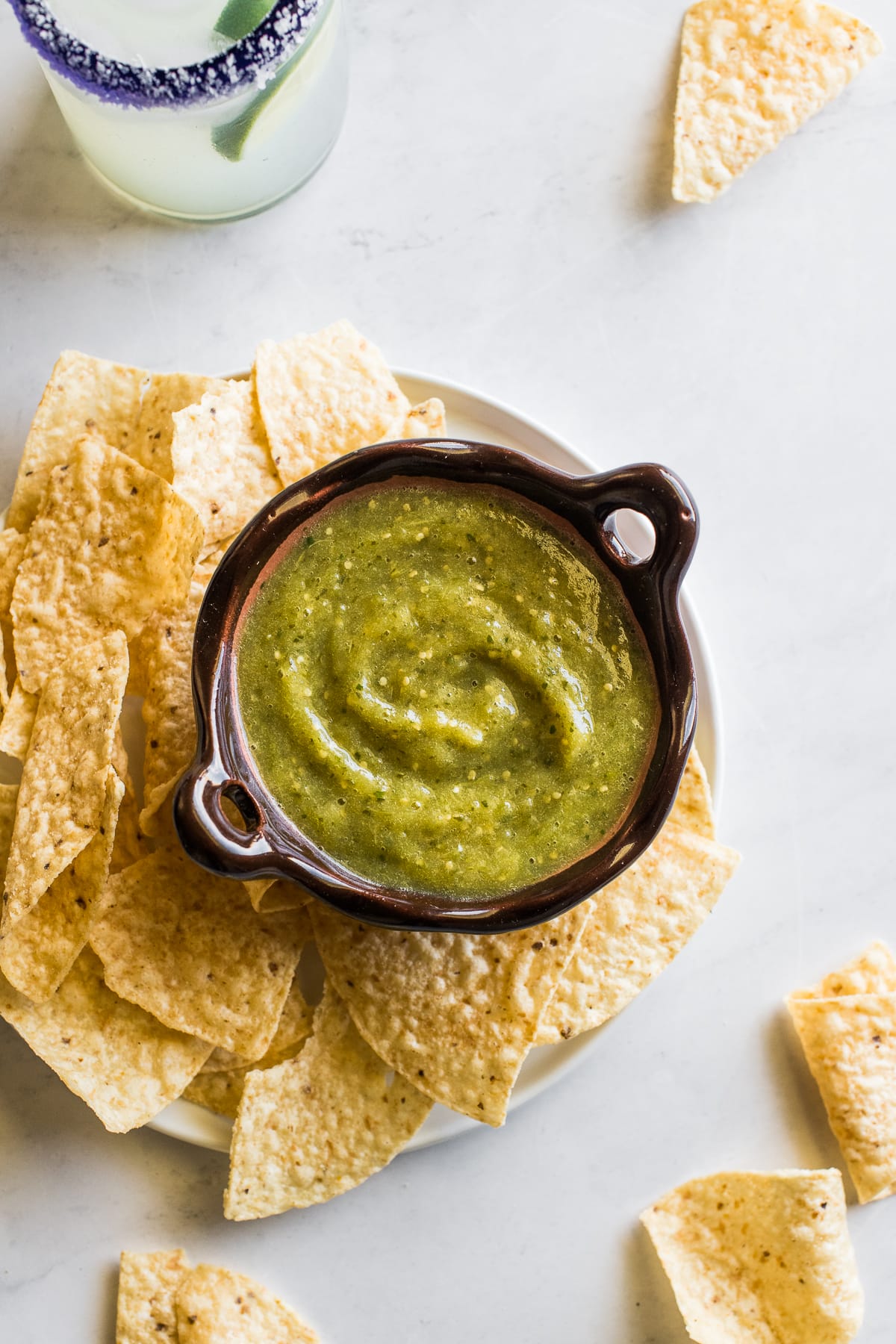 Salsa verde on a table next to tortilla chips.