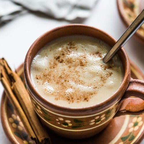 A cup of atole in a Mexican clay mug topped with ground cinnamon.