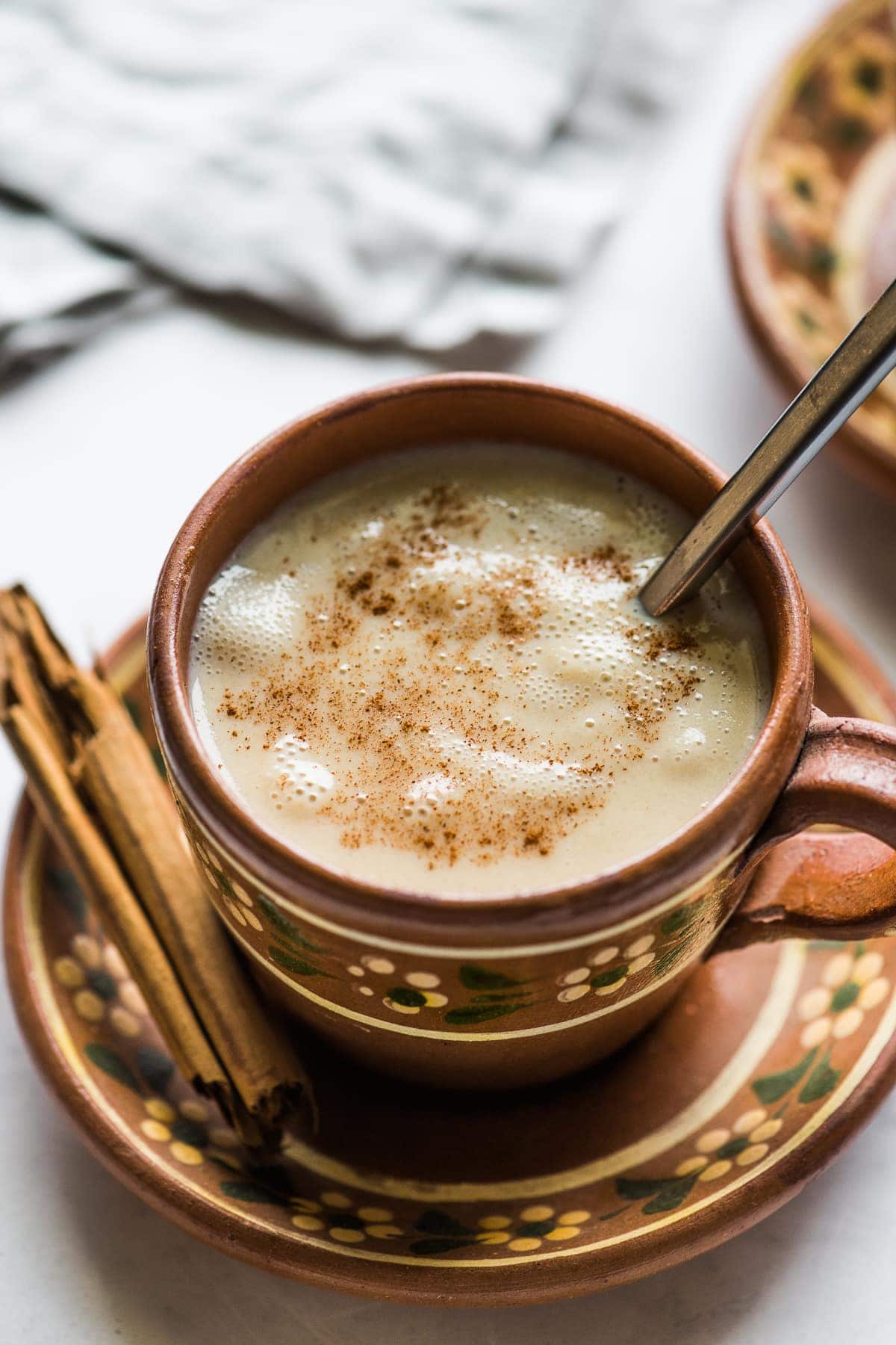 A cup of atole in a Mexican clay mug topped with ground cinnamon.