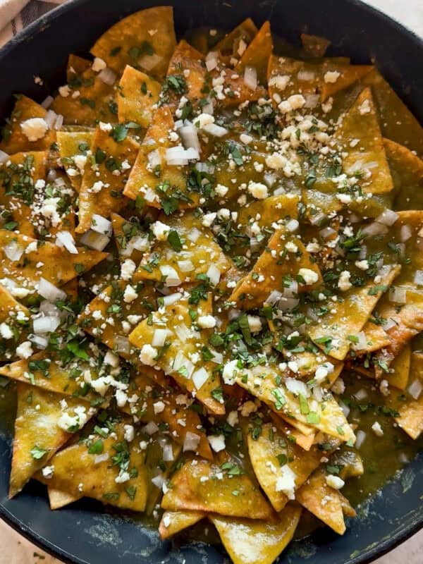 Chilaquiles verdes, aka green chilaquiles, in a skillet topped with ciantro, onion, and cotija cheese.