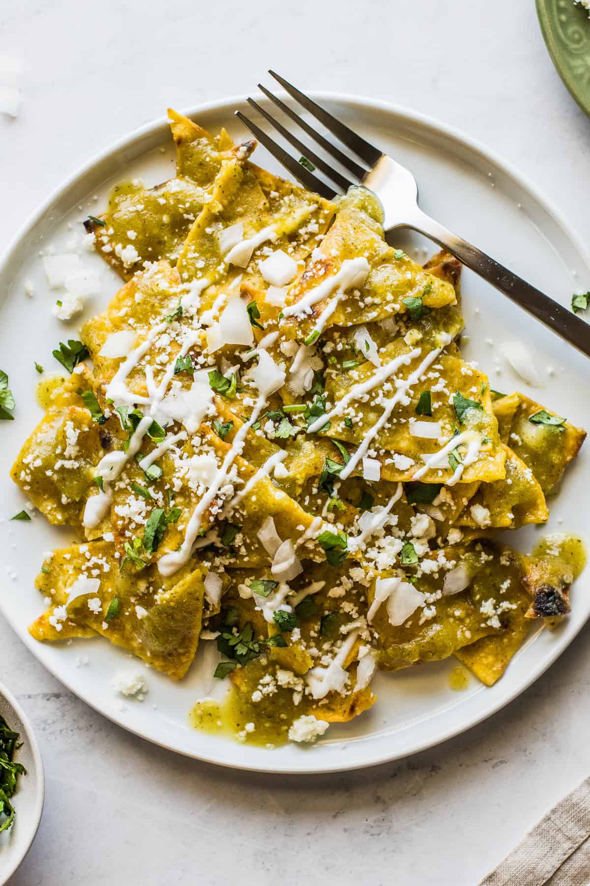Chilaquiles verdes (green chilaquiles) on a white plate topped with crema, cotija, onion, and cilantro