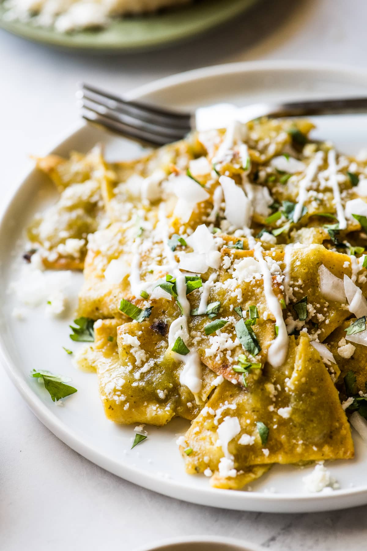 Chilaquiles verdes cubiertos con crema, cilantro y cebolla.