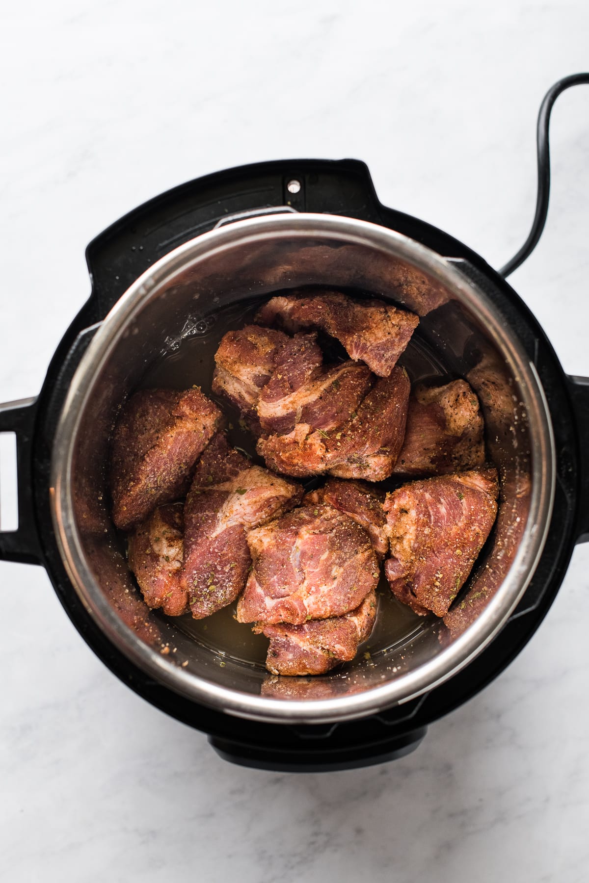 Seasoned chunks of pork shoulder in an Instant Pot pressure cooker.