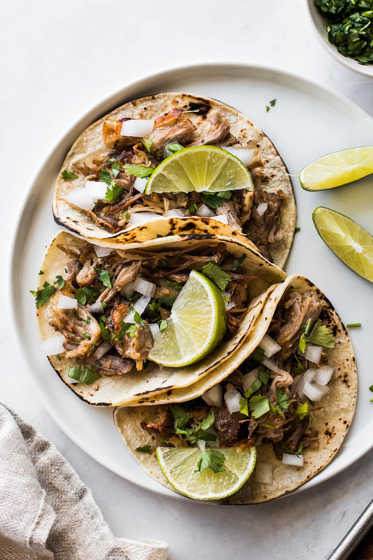 Instant Pot carnitas in tacos topped with onions, cilantro, and lime wedges.