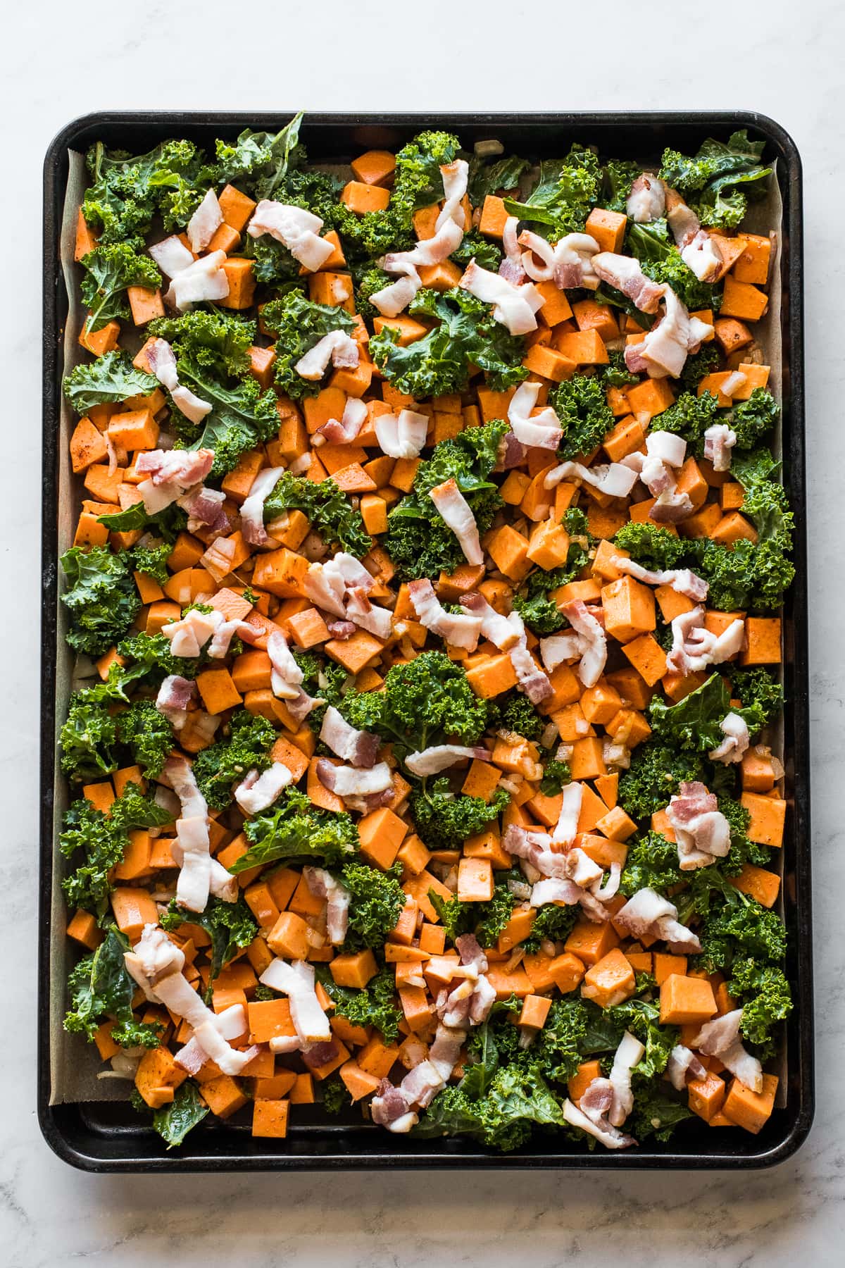 Sweet potatoes, kale, and bacon on a sheet pan.