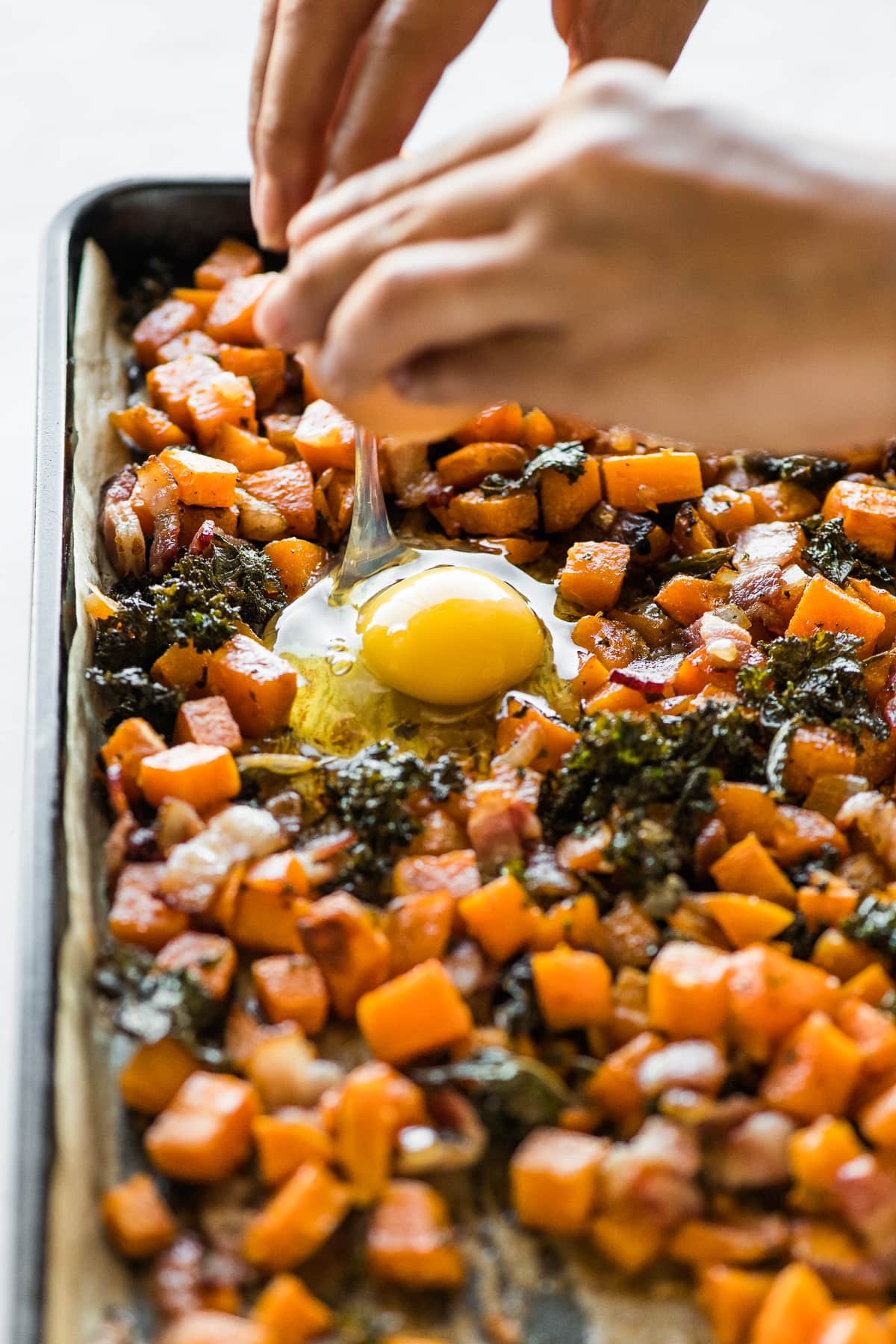 An egg being cracked onto a sheet pan for breakfast.