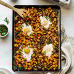 Sheet pan eggs and breakfast hash on a table next to plates.