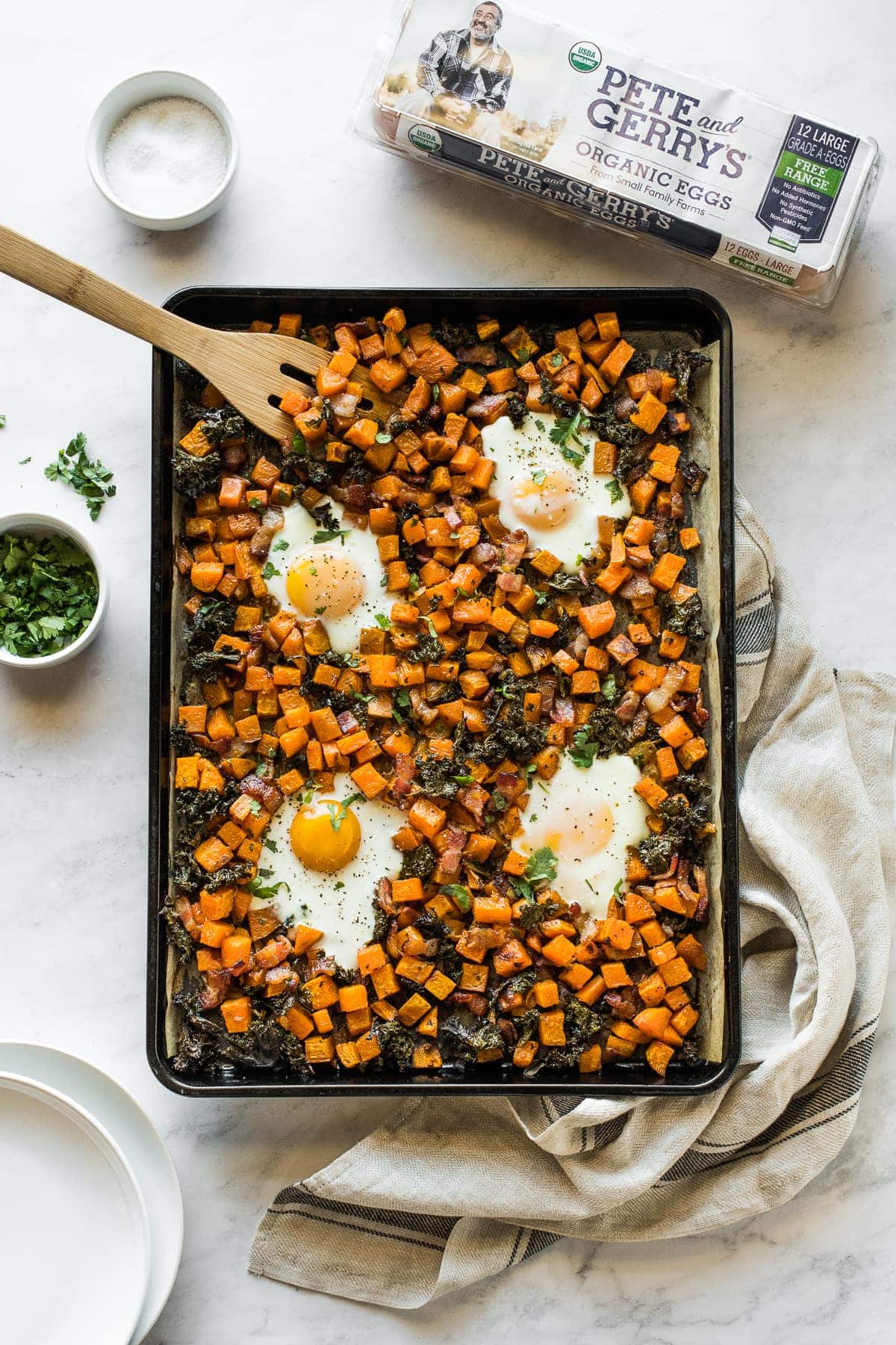 Sheet pan eggs and breakfast hash on a table next to plates.