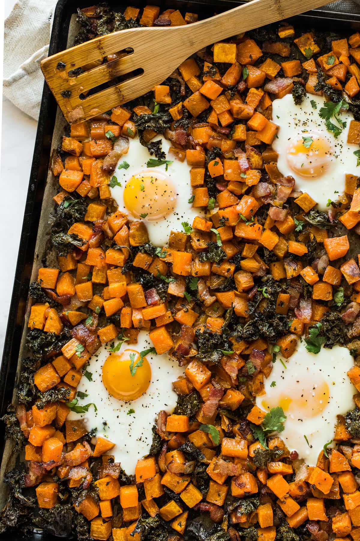 Cooked eggs on a sheet pan with sweet potatoes, kale, and spices.