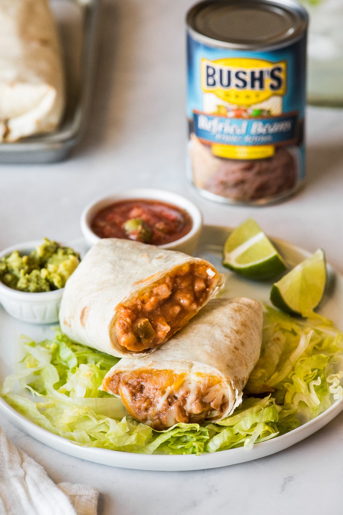 A bean and cheese burrito cut in half and stacked on a plate with lettuce.
