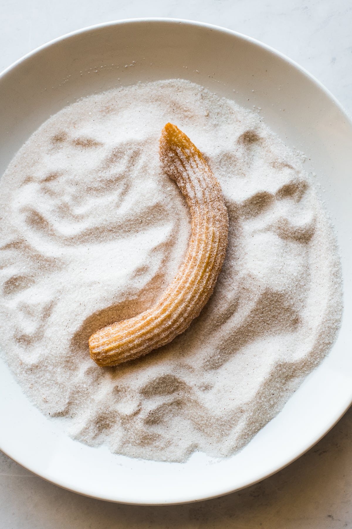 Churros being covered in cinnamon sugar coating.