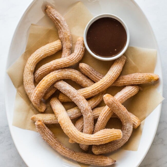 Churros covered in cinnamon sugar with a ramekin of chocolate sauce.