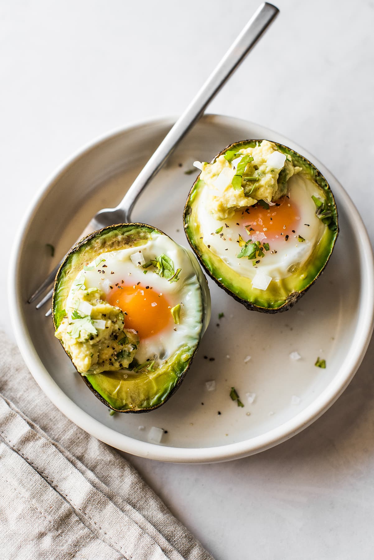 Baked eggs in avocado on plate garnished with cilantro.