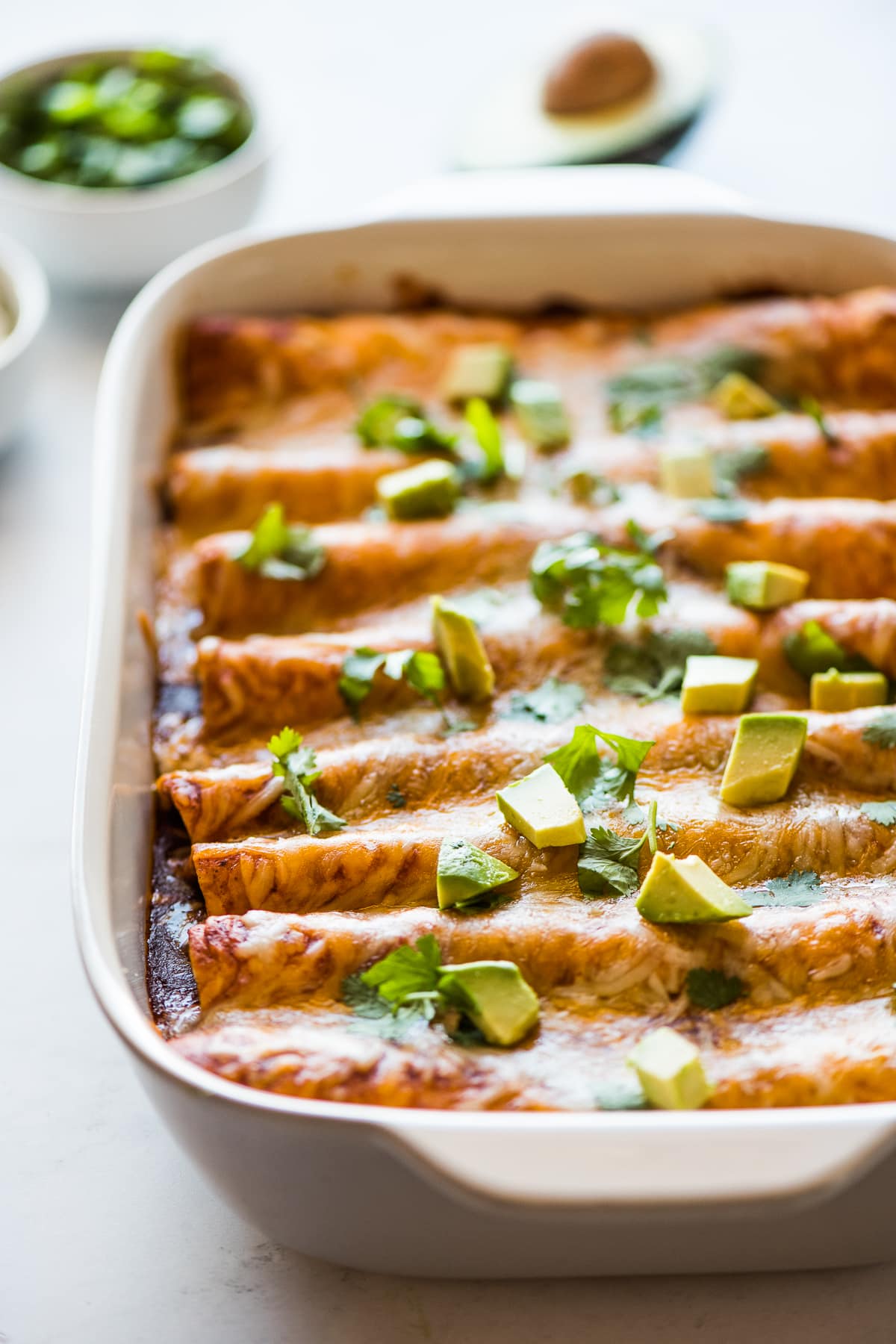 Black bean enchiladas topped with diced avocados and cilantro in a baking dish.