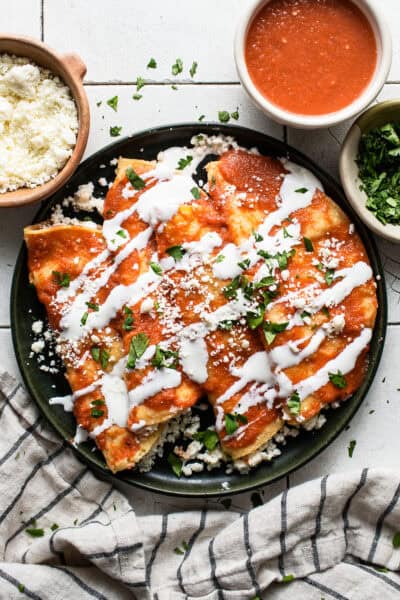 Entomatadas on a plate garnished with Mexican crema, cotija cheese, and cilantro.
