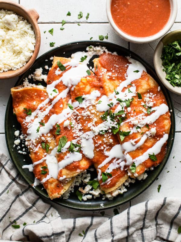 Entomatadas on a plate garnished with Mexican crema, cotija cheese, and cilantro.