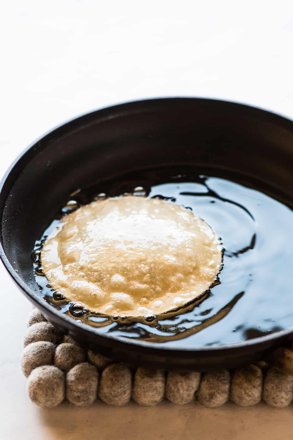 A corn tortilla lightly shallow frying in a skillet of vegetable oil.