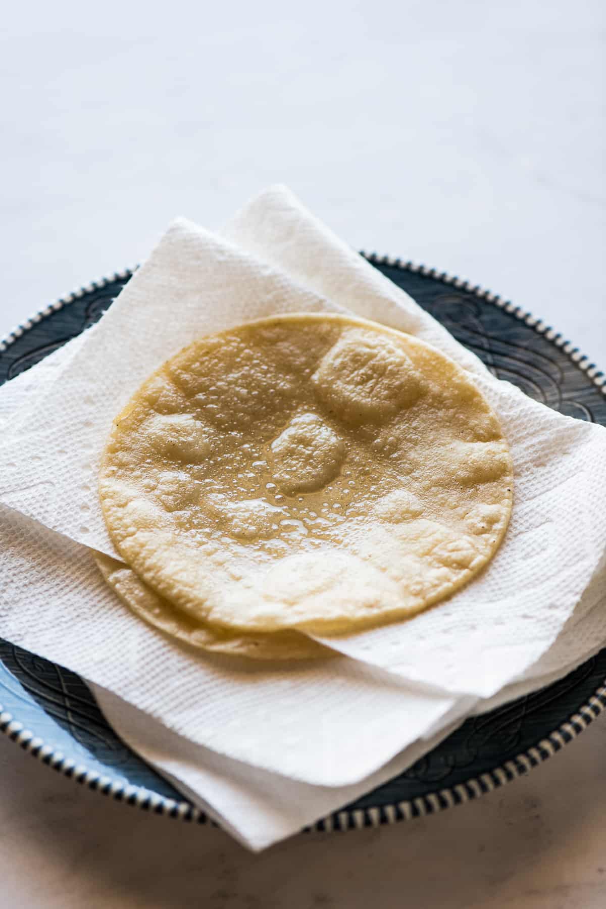 Fried corn tortillas draining on a plate with paper towels.