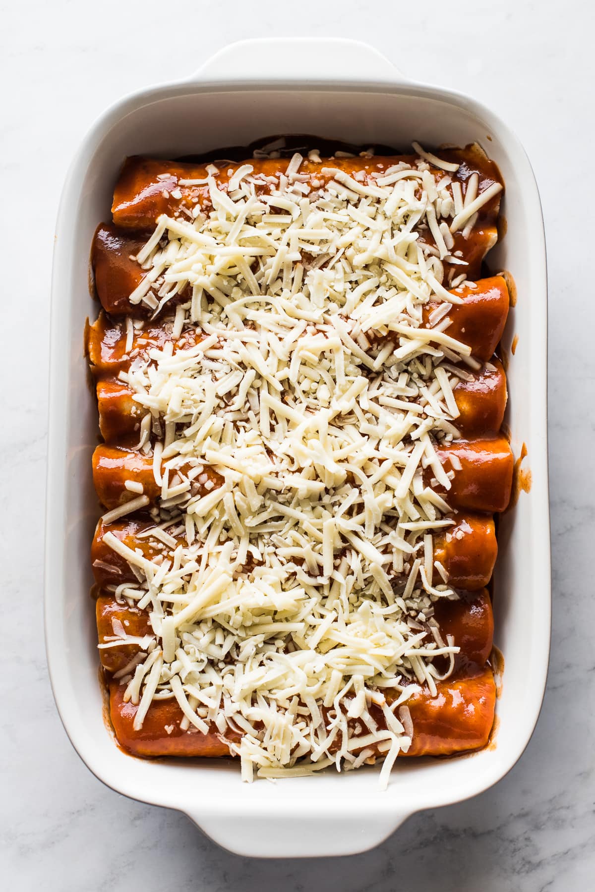 Turkey enchiladas in a baking dish topped with shredded cheese.
