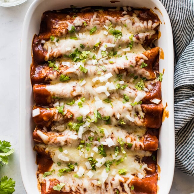 Turkey enchiladas in a baking dish topped with cilantro and onions.